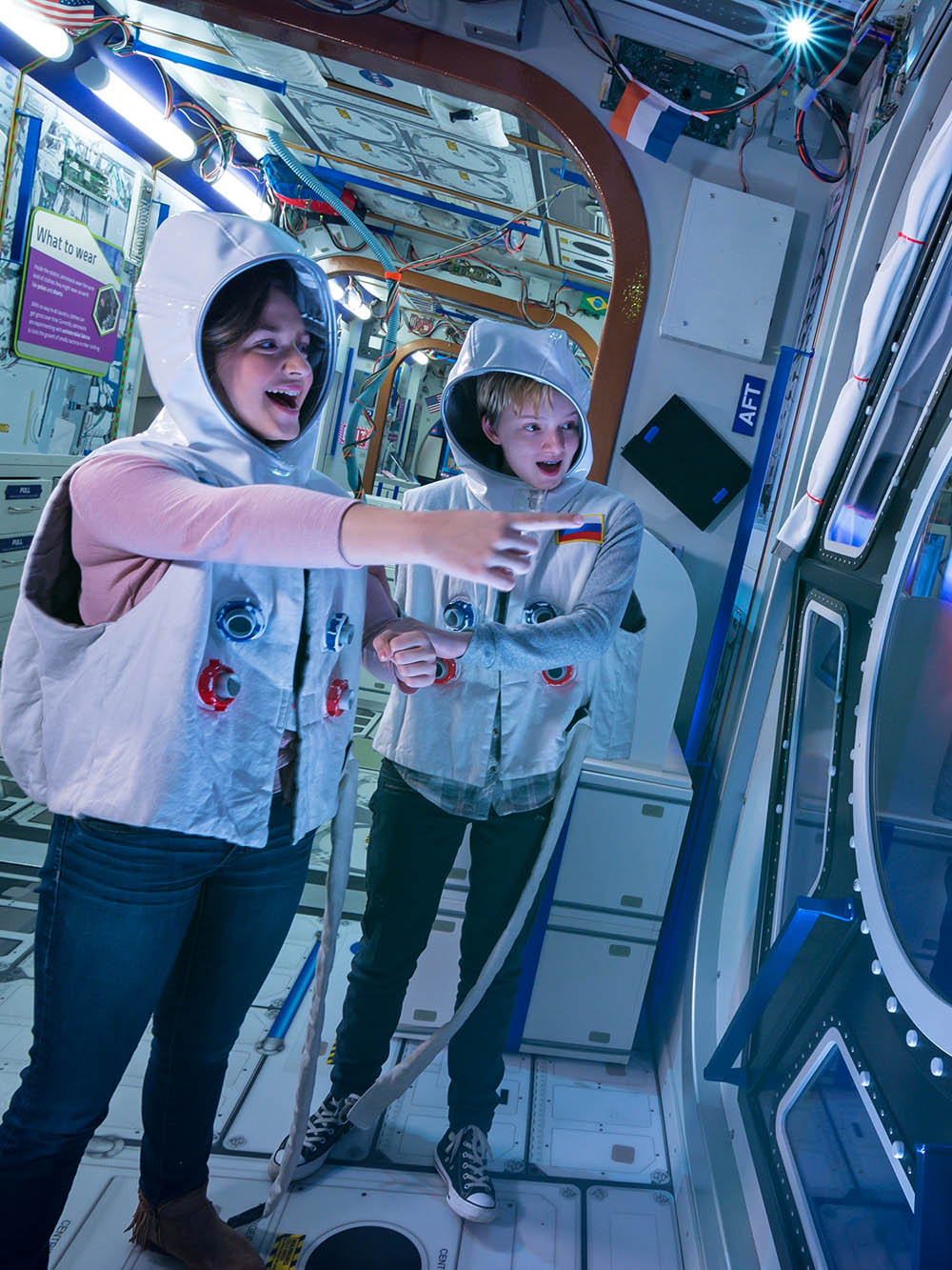 People wearing astronaut costumes and pointing out a window. It looks like they're on a space station.